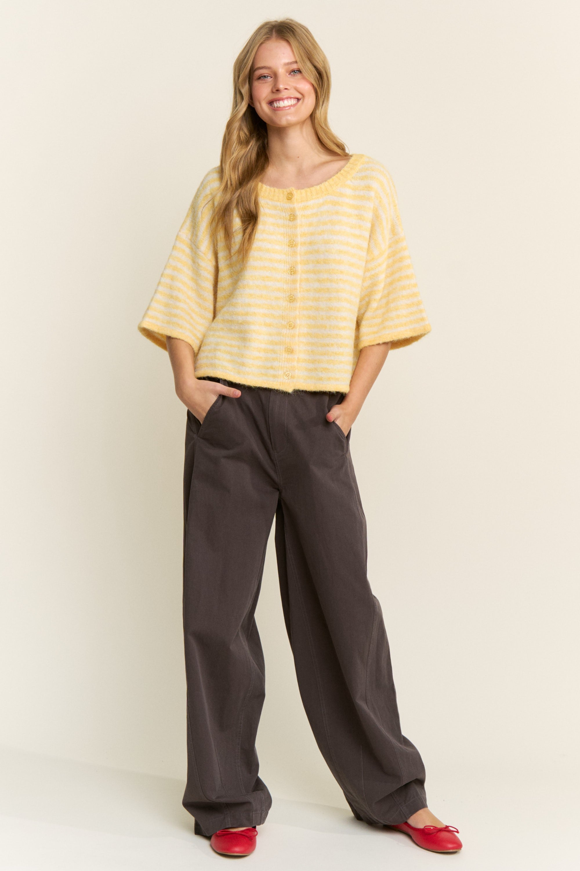 Woman wearing a yellow striped shirt and dark pants against a white background